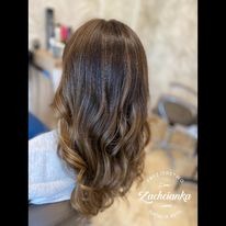 Kobieta z tyłu, prezentująca brązowe włosy z refleksami, delikatnie pofalowane, widoczne kosmetyki i sprzęt w tle.