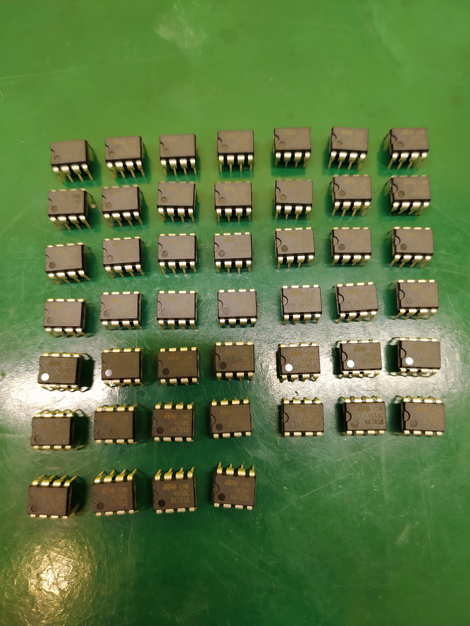 Równomiernie ułożone układy scalone DIP-8 na zielonym tle, widoczne oznaczenia '4558C KK7818' oraz logo producenta.