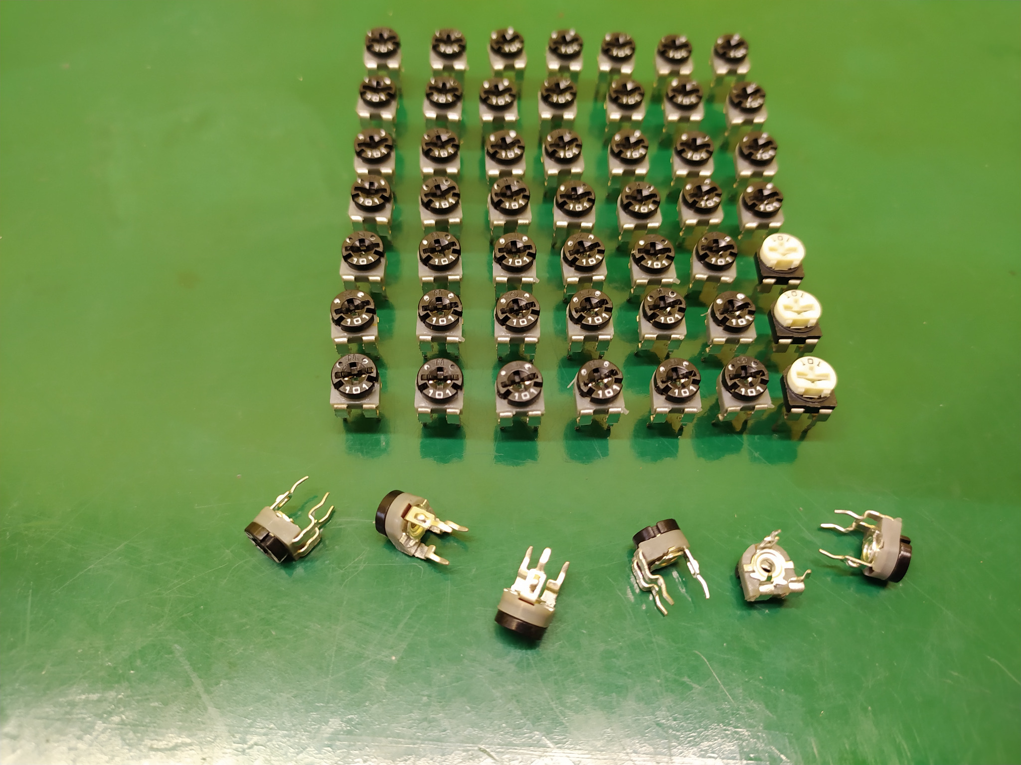 Uporządkowany układ potencjometrów montażowych na zielonym tle, kilka sztuk leży poza formacją.