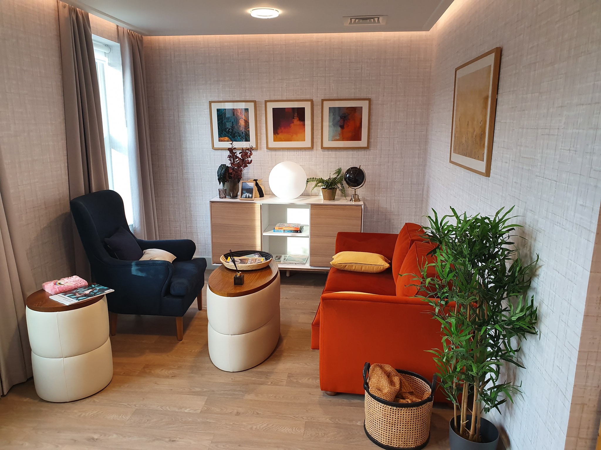 Jasne wnętrze pokoju dziennego z pomarańczową sofą, granatowym fotelem i dekoracjami w stylu skandynawskim, oświetlone listwami LED.