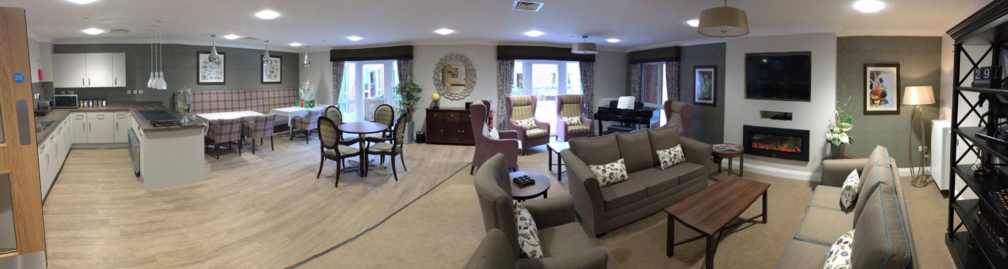 Panoramiczne ujęcie przestronnego wnętrza domu spokojnej starości z kuchnią, jadalnią i salonem, w neutralnej kolorystyce, z elementami dekoracyjnymi i meblami.