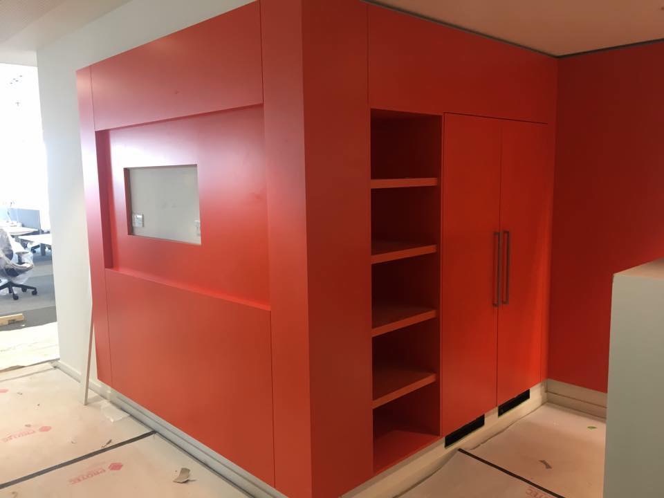 Pomarańczowa zabudowa meblowa z półkami i szafkami, widoczna w biurze w Świdnicy, z oknem wbudowanym w ścianę.