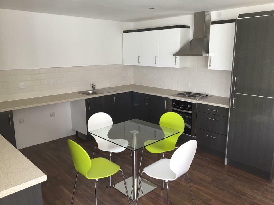 Nowoczesna kuchnia z ciemnymi dolnymi szafkami, białymi górnymi szafkami, szklanym stołem i zielono-białymi krzesłami na drewnianej podłodze.