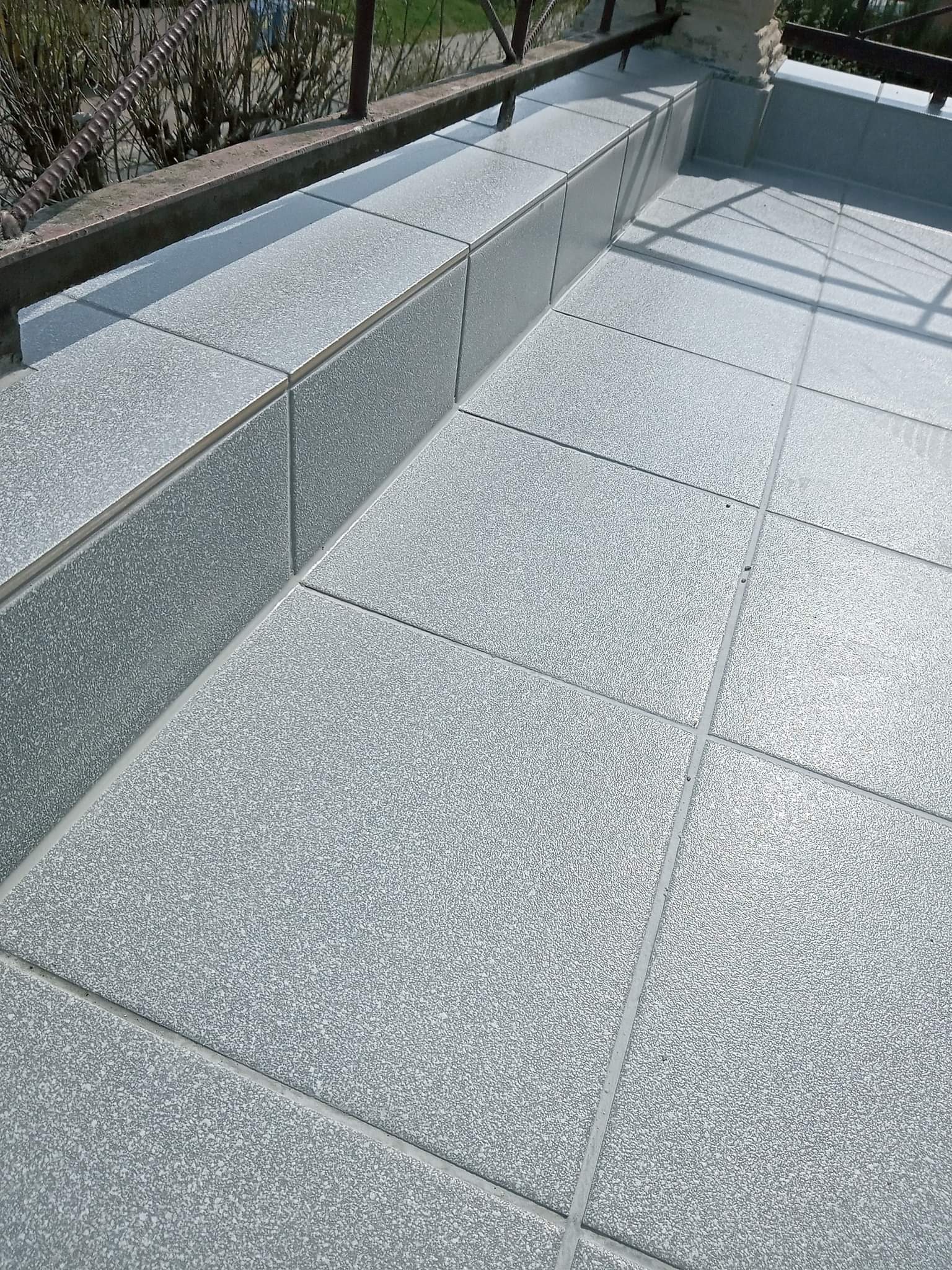 Szare, matowe płytki gresowe na balkonie, ułożone równo z wąskimi fugami, widoczne barierki balkonowe w tle.