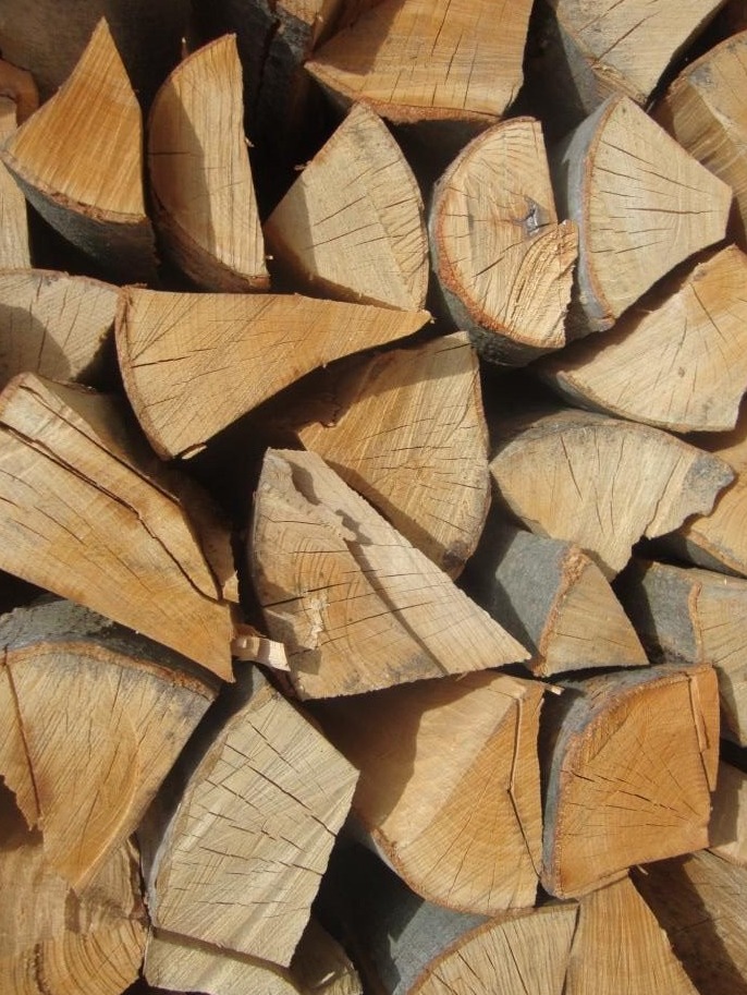 Ułożone, porąbane kawałki drewna z widocznymi słojami i korą, przygotowane do spalenia w kominku.