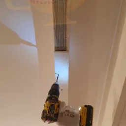 Montaż metalowego profilu sufitowego za pomocą wkrętarki DeWalt, widoczna ręka w białej rękawicy ochronnej.