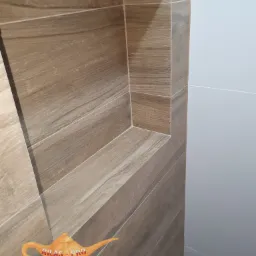 Narożna półka w łazience wyłożona płytkami imitującymi drewno, sąsiadująca z gładką, jasną ścianą.