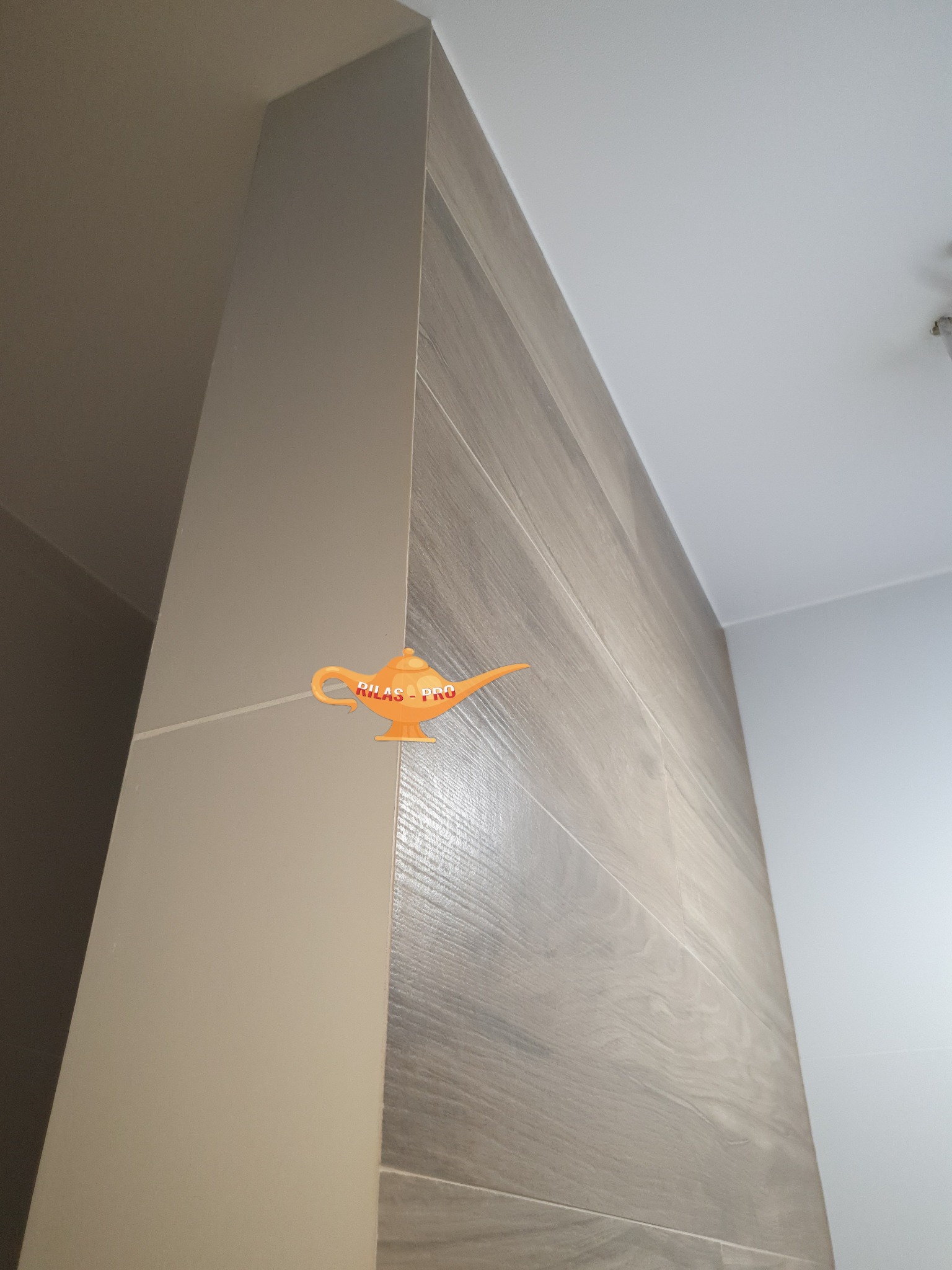 Narożnik łazienki wykończony płytkami imitującymi drewno oraz pomalowany na jasny beż, widok od dołu.