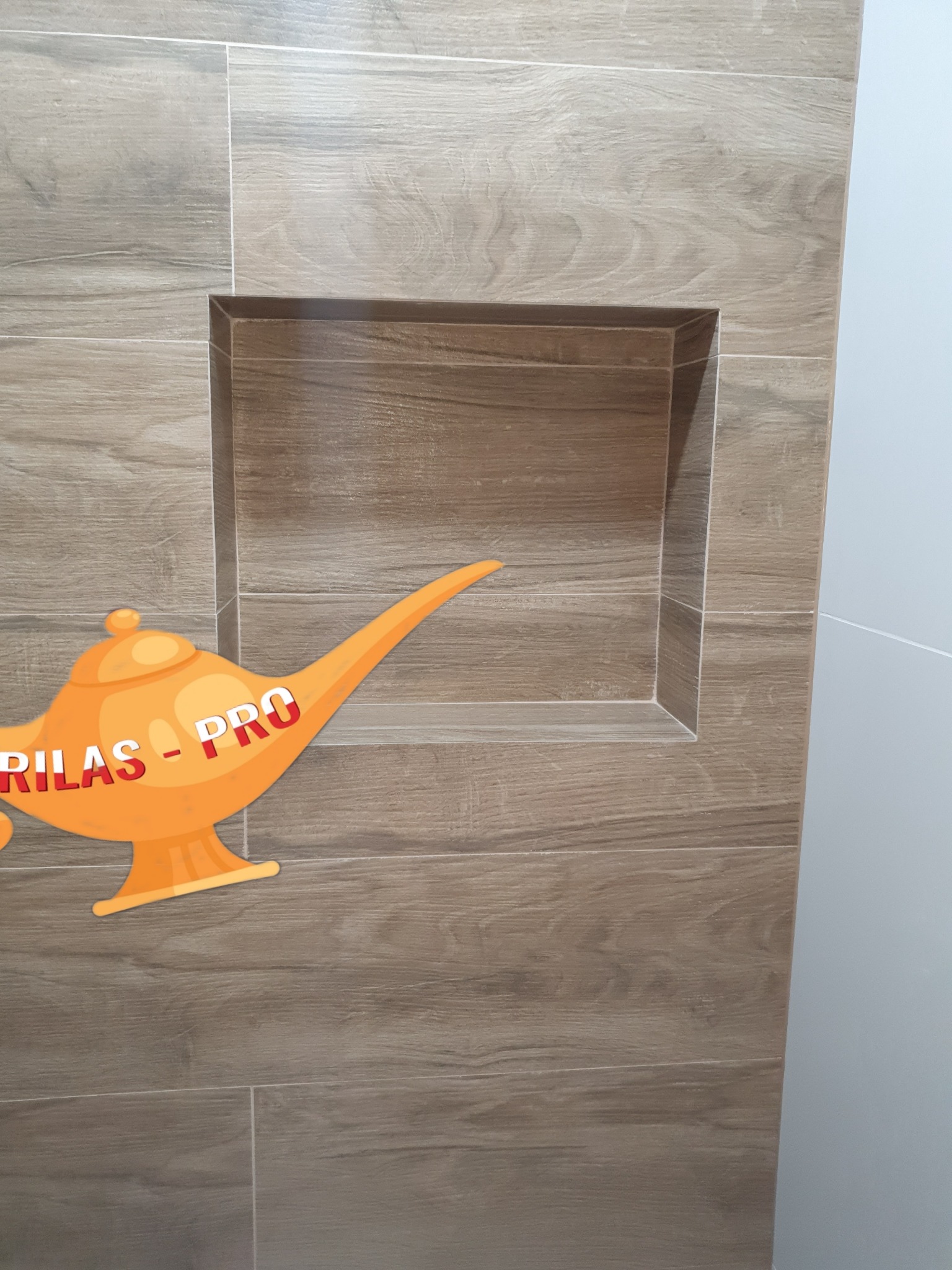 Narożna wnęka wyłożona płytkami imitującymi drewno w łazience, na płytkach naklejka w kształcie lampy Aladyna z napisem RILAS-PRO.