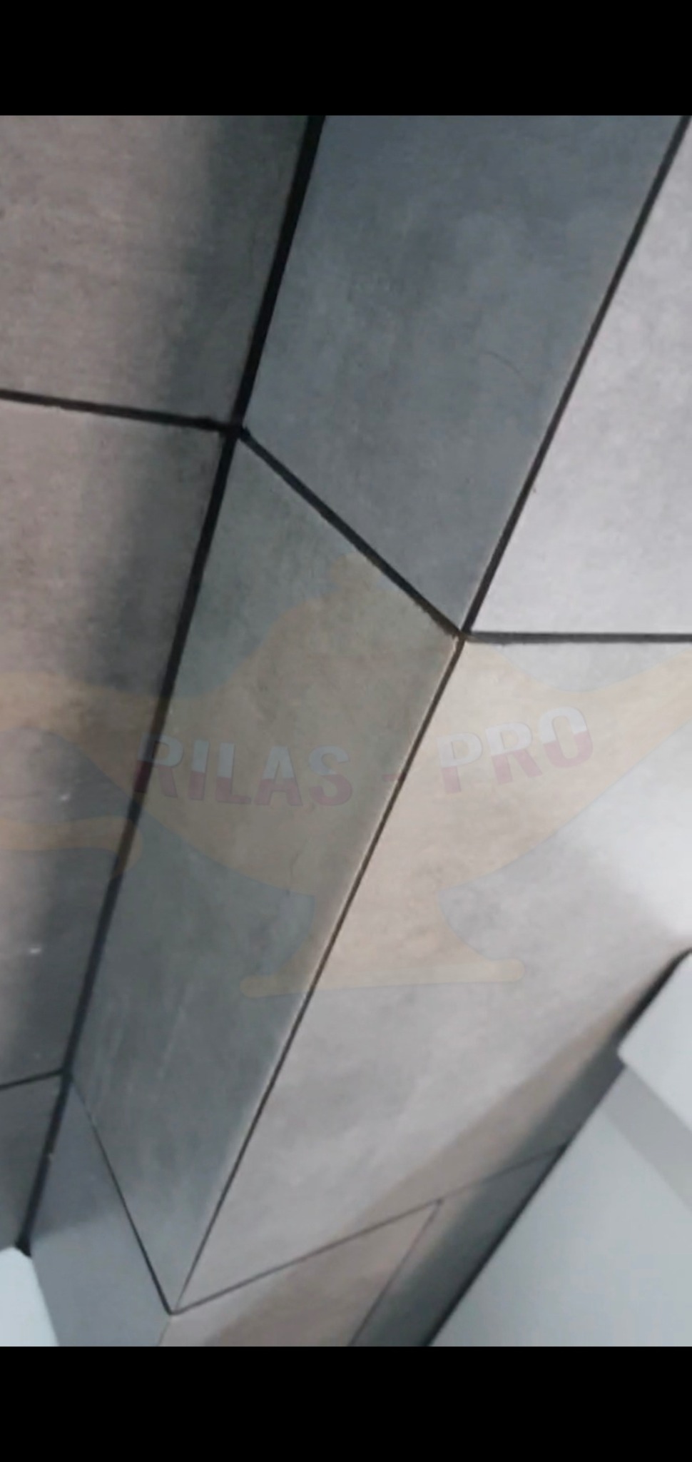 Świeżo położone, szare, matowe płytki na ścianie, widoczne spoiny i fragment białej ściany z prawej strony.