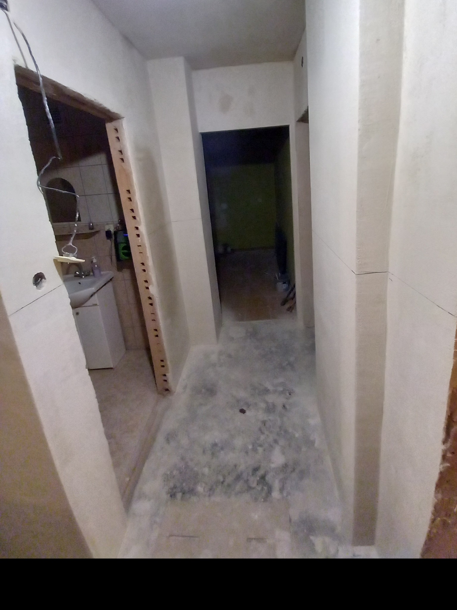 Korytarz w trakcie prac wykończeniowych, widoczne surowe ściany i futryny drzwiowe przed obróbką, w tle widoczna łazienka z białą umywalką.