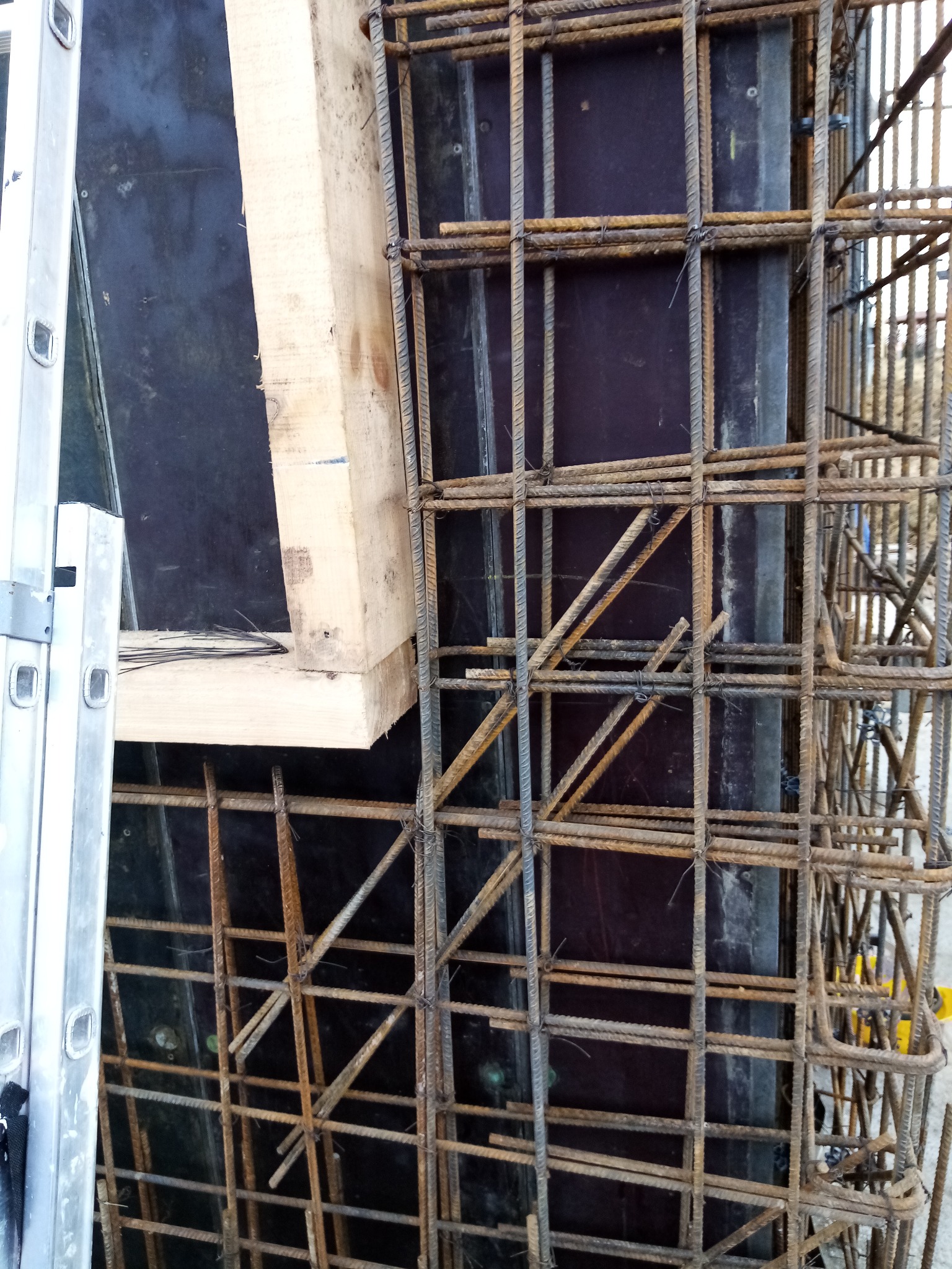 Zbrojenie kolumny żelbetowej z deskowaniem, widoczna drabina aluminiowa w tle.