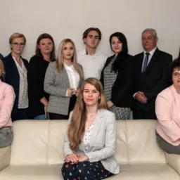 Zespół pracowników firmy ubezpieczeniowej pozuje do zdjęcia grupowego w biurze, kobiety w marynarkach i mężczyźni w koszulach i garniturach.