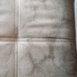 EVELYN Firma Sprzątająca Ewelina Belc - Szczegółowe ujęcie tapicerki sofy z widocznymi plamami i przeszyciami, ukazujące potrzebę profesjonalnego czyszczenia. Tekstura materiału z bliska.