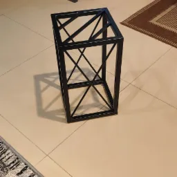 Metalowa konstrukcja w kształcie sześcianu z wewnętrznymi przekątnymi, wykonana z czarnych profili, stoi na jasnych płytkach podłogowych w pomieszczeniu. W tle widoczne meble kuchenne.