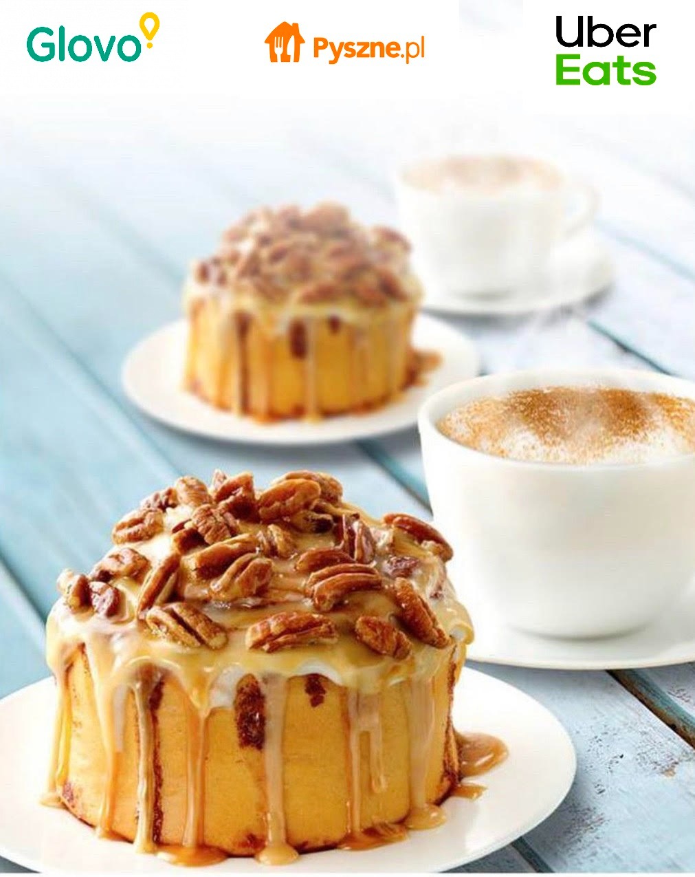 Dwa ciastka cynamonowe z orzechami pekan i sosem karmelowym na białych talerzykach, obok filiżanki kawy z pianką, z logo Glovo, Pyszne.pl i Uber Eats u góry.