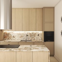 Paulina Teodorczyk - Architektura Wnętrz - Beżowa kuchnia z wyspą i marmurowym blatem, oświetlona listwą LED pod szafkami. Minimalistyczny okap i dekoracyjne, okrągłe elementy na ścianie.