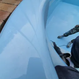 Malowanie wnętrza niebieskiego zbiornika wodnego, widoczne krople farby i częściowo sylwetka pracownika w ubraniu roboczym.