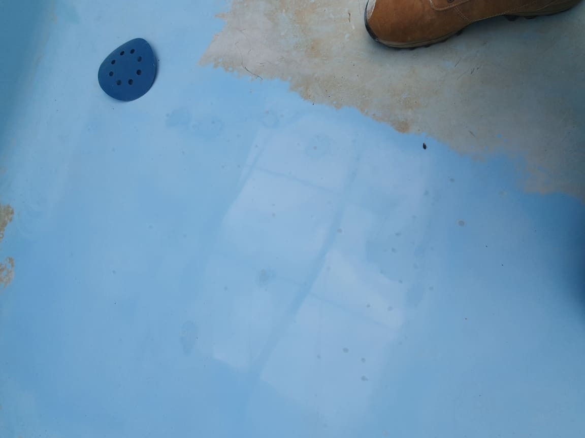 Błękitna powierzchnia w trakcie czyszczenia, widoczny fragment buta roboczego w prawym górnym rogu i niebieski element z otworami po lewej stronie.