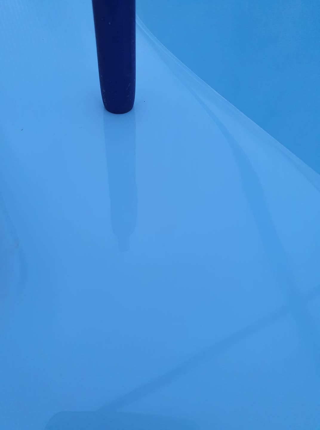 Niebieska powierzchnia z odbiciem ciemnego przedmiotu, przypominająca wodę w basenie lub oczku wodnym