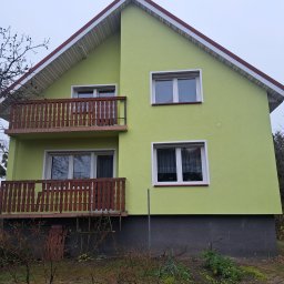 Dawid Drost - Dwukondygnacyjny dom z balkonami, pomalowany na jasnozielono, z ciemnoszarą podmurówką i brązowymi balustradami. Widok na elewację w pochmurny dzień.