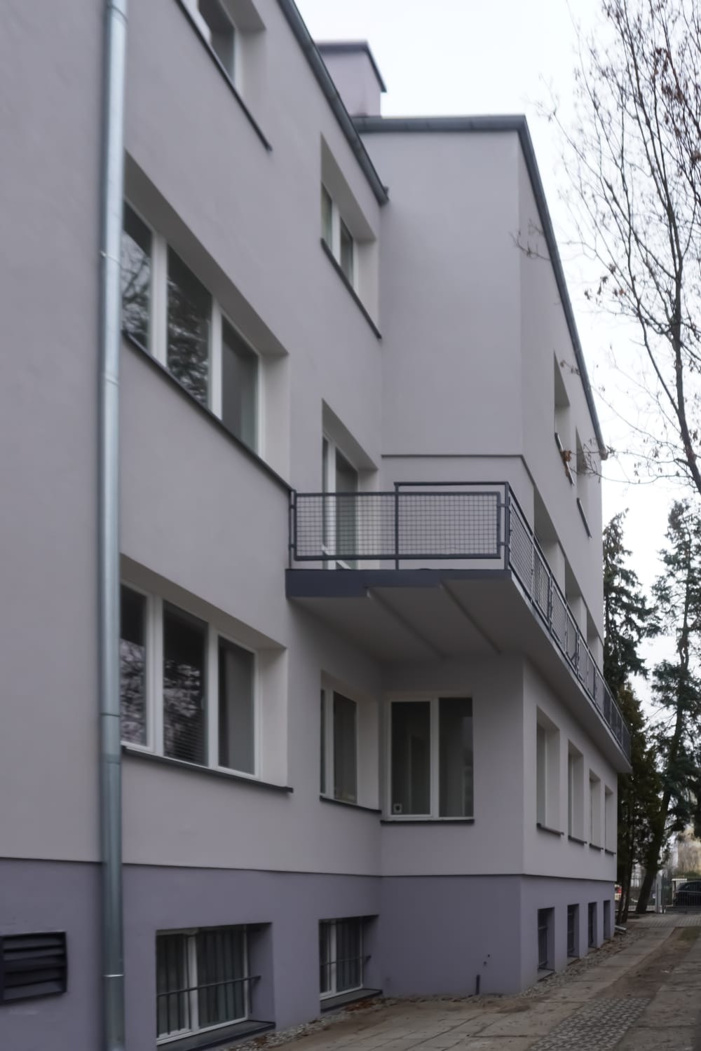 Budynek wielorodzinny po renowacji elewacji, z balkonami i szarą, dwukolorową fasadą. Widoczne okna z białymi ramami i rynna spustowa.