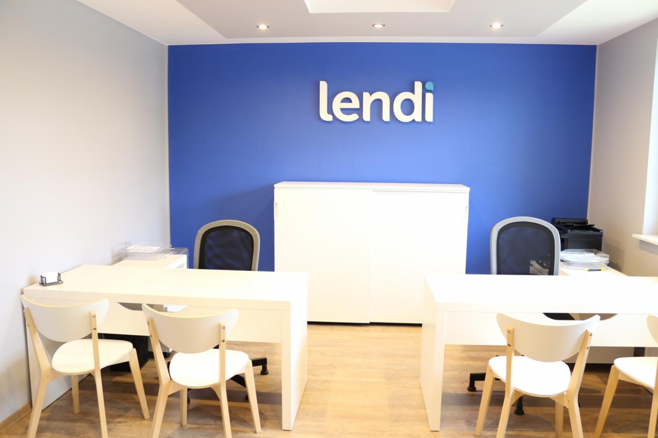 Jasne biuro z błękitną ścianą, logo 'lendi', białymi biurkami i krzesłami, minimalistyczny design.
