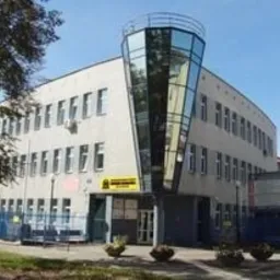 Budynek szkoły lub centrum szkoleniowego z charakterystyczną, przeszkloną wieżyczką na rogu, widoczny szyld informacyjny przy wejściu.