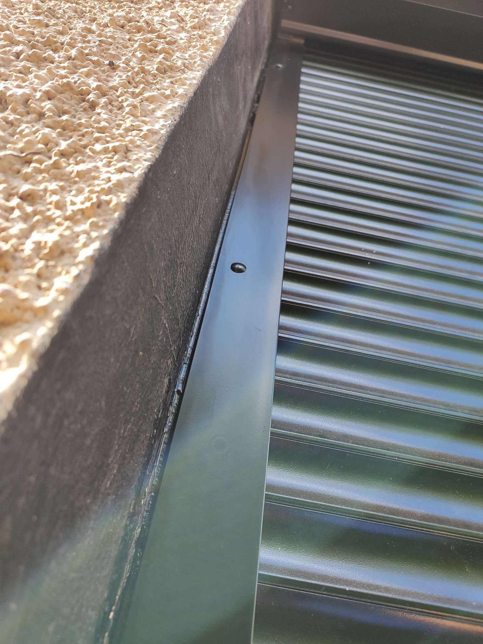 Fragment elewacji z zamontowaną, zamkniętą roletą zewnętrzną w Łodzi, widoczny detal mocowania do ściany o nierównej fakturze.