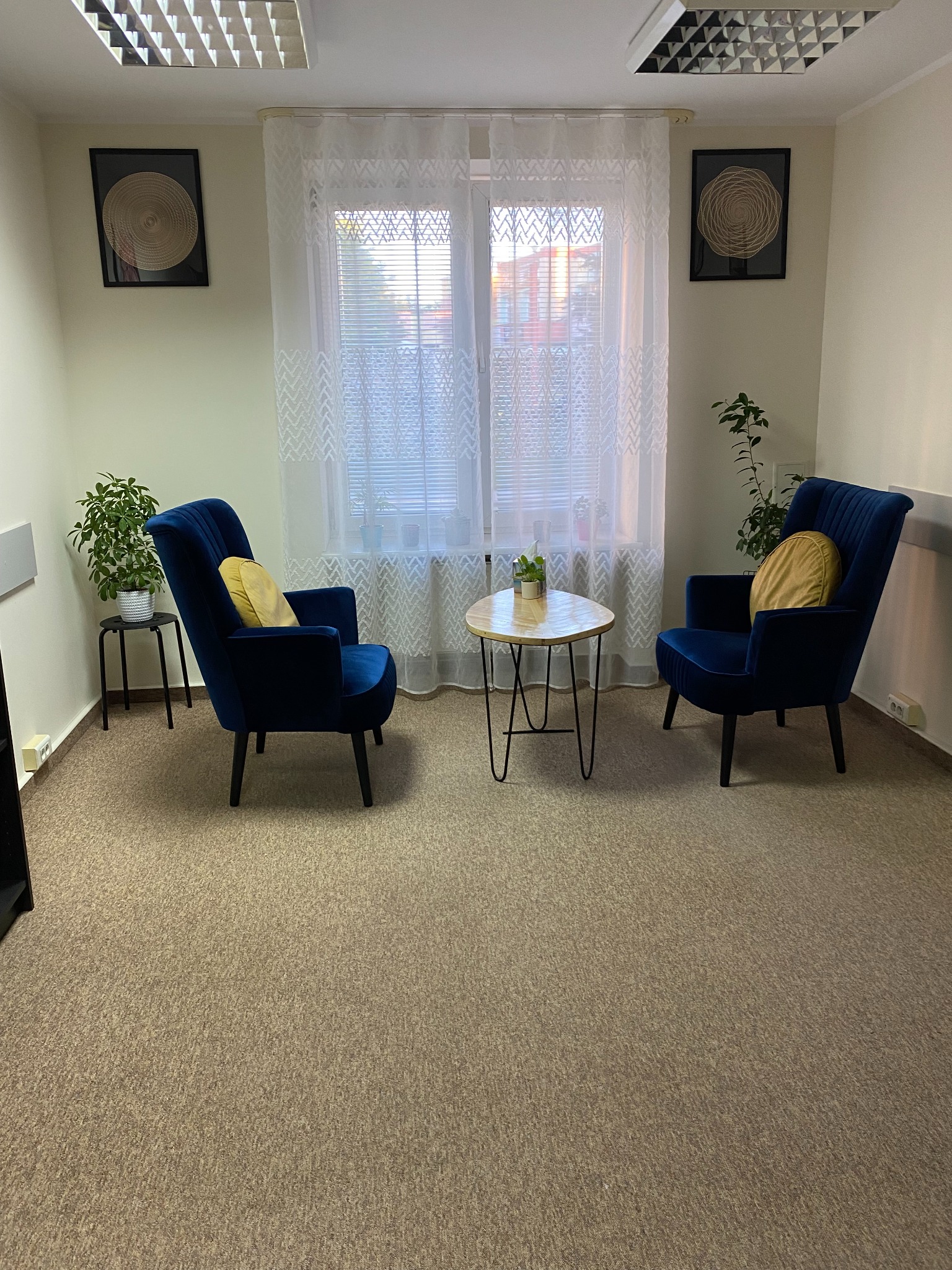 Gabinet z dwoma granatowymi fotelami, okrągłym stolikiem kawowym i dekoracjami ściennymi.