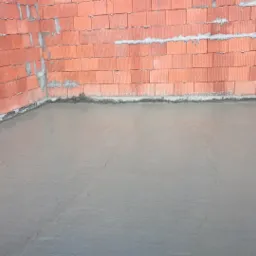 Wylany betonowy podkład podłogowy w surowym wnętrzu z czerwonej cegły, widoczne ślady po łatach niwelacyjnych.