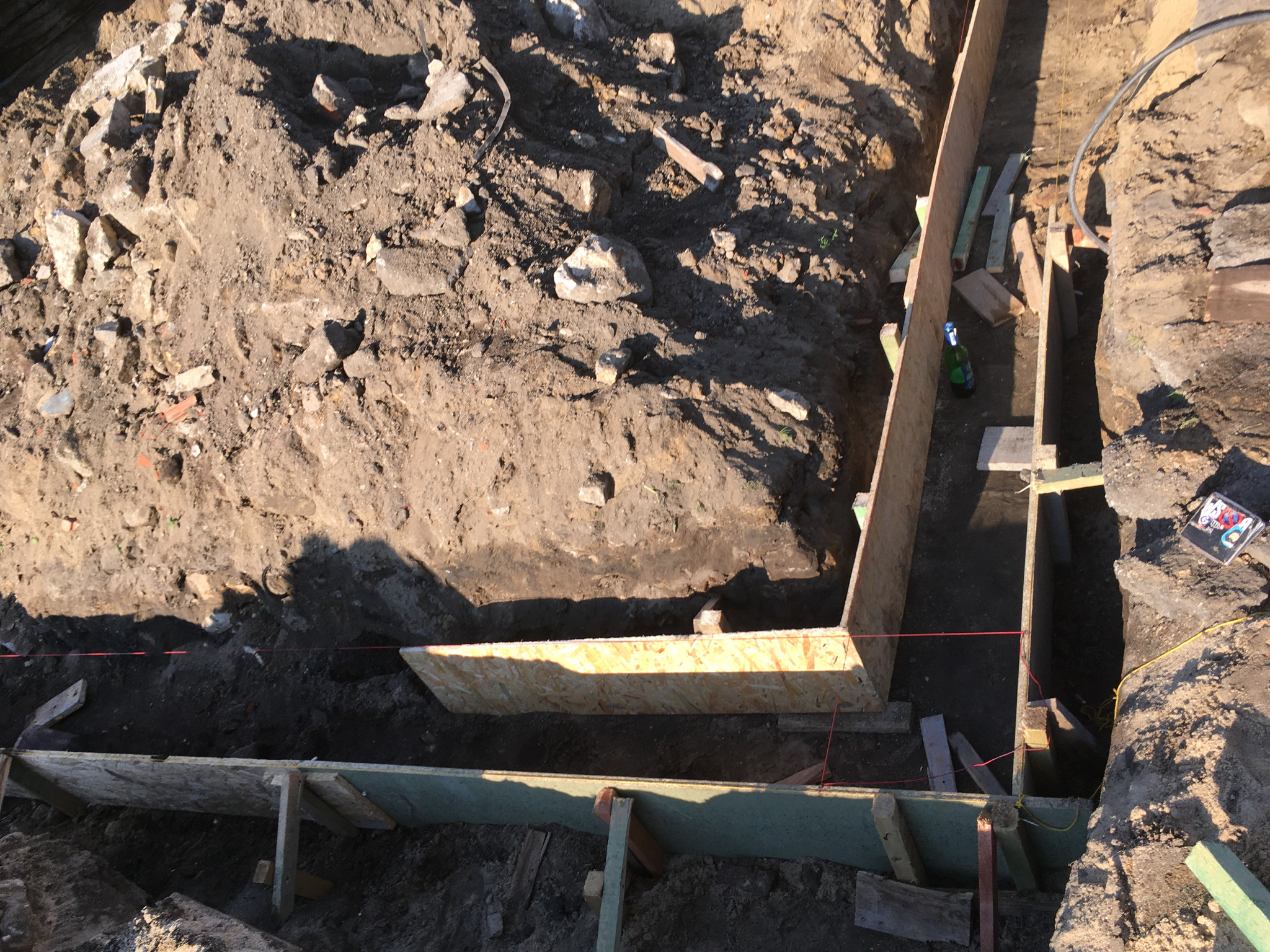 Ziemny wykop z drewnianym szalunkiem przygotowanym pod wylanie fundamentów, widok z góry, w tle gruz i ziemia.