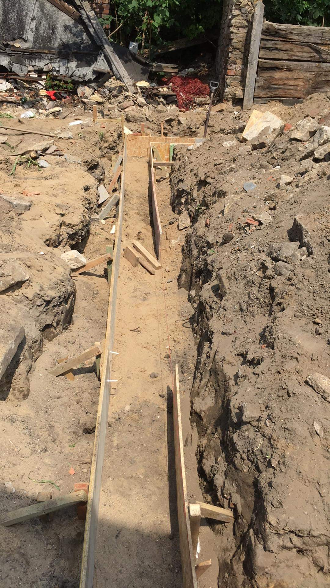 Wykop fundamentów z drewnianym szalunkiem, widoczne nierówne ściany wykopu i gruz na powierzchni.