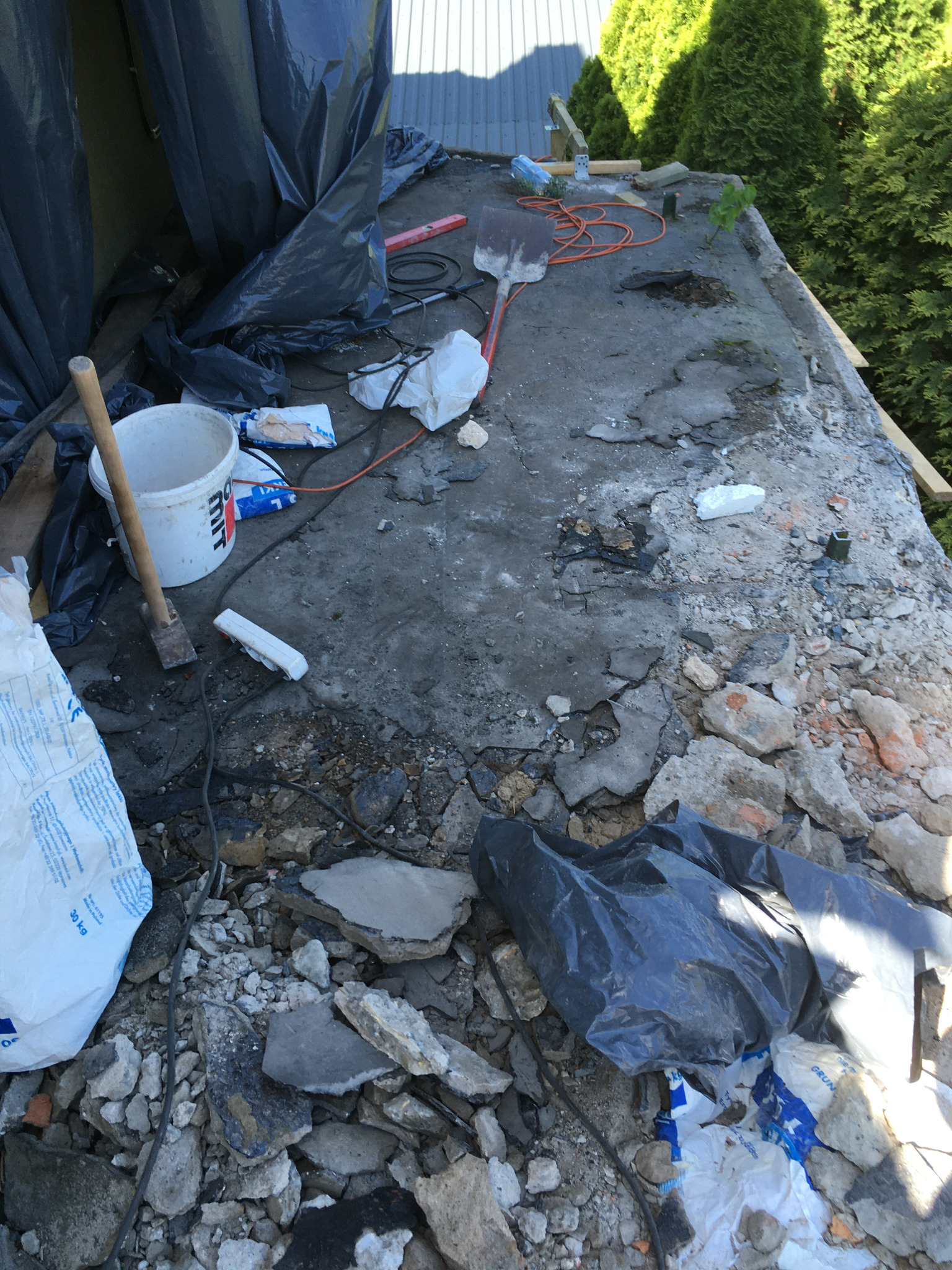 Przygotowanie do remontu dachu: gruz, worki z zaprawą, narzędzia budowlane i folia ochronna na powierzchni dachu.