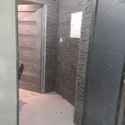 Wnętrze korytarza z wykończeniem ściany z szarej cegły dekoracyjnej, widoczna biała skrzynka elektryczna, drzwi wejściowe i fragment drzwi wewnętrznych z ciekawskim psem.