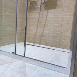 REMONTER Firma transportowo-budowlana Krzysztof Gleba - Beżowa łazienka z kabiną prysznicową typu walk-in, widoczne płytki imitujące trawertyn na ścianach i podłodze, oraz odpływ liniowy.