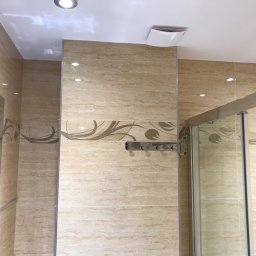 REMONTER Firma transportowo-budowlana Krzysztof Gleba - Wykończona łazienka z beżowymi, marmurkowymi płytkami z dekoracyjnym pasem, kabina prysznicowa ze szklanymi drzwiami, oświetlenie punktowe w suficie i metalowy wieszak na ręczniki.