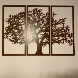 Dekoracja ścienna: trzy drewniane panele przedstawiające stylizowany, wycięty laserowo motyw drzewa na białym tle ściany.