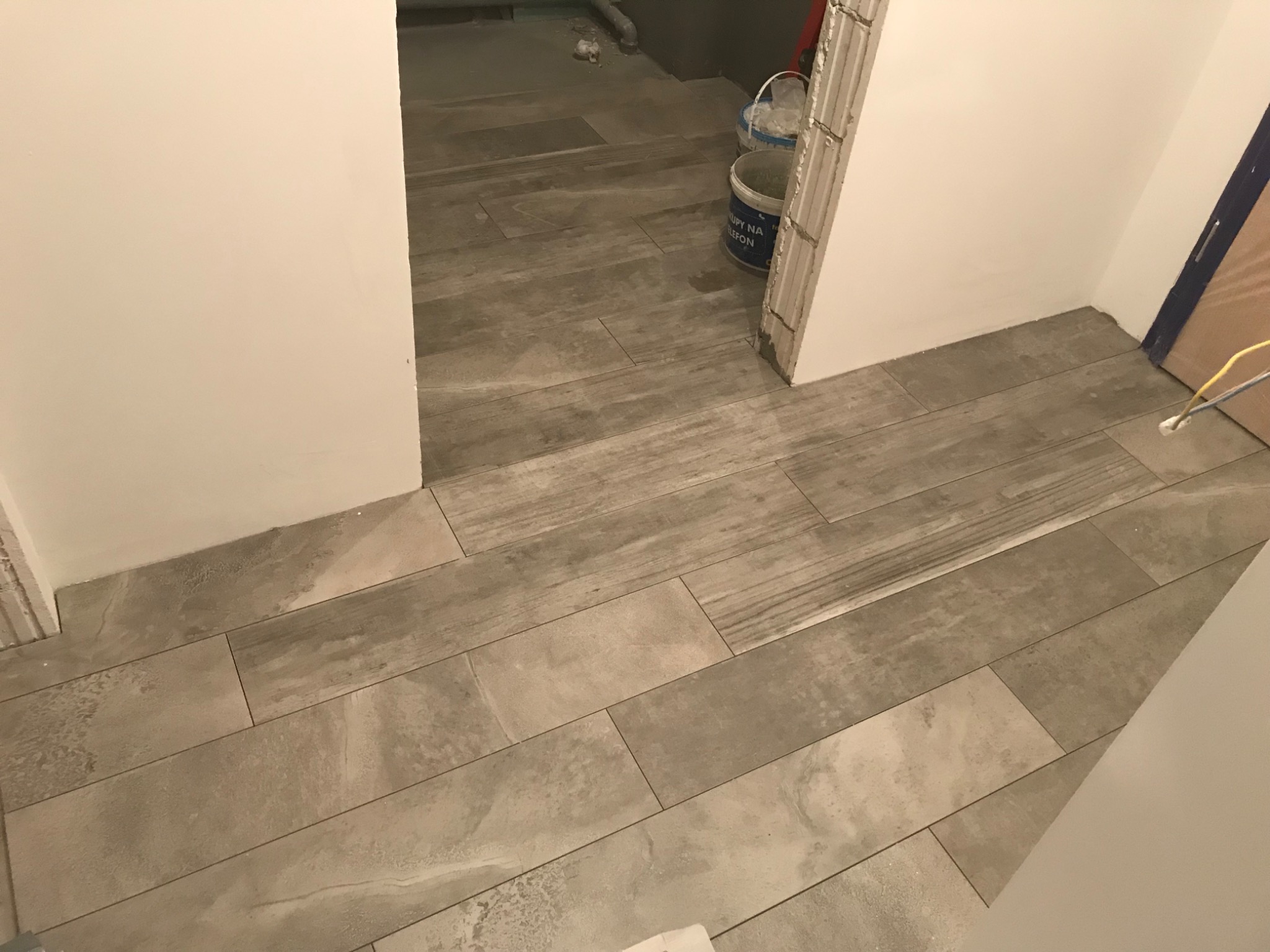 Ułożona podłoga z płytek imitujących drewno w trakcie remontu łazienki, widoczne wiaderka z farbą i wystające kable.
