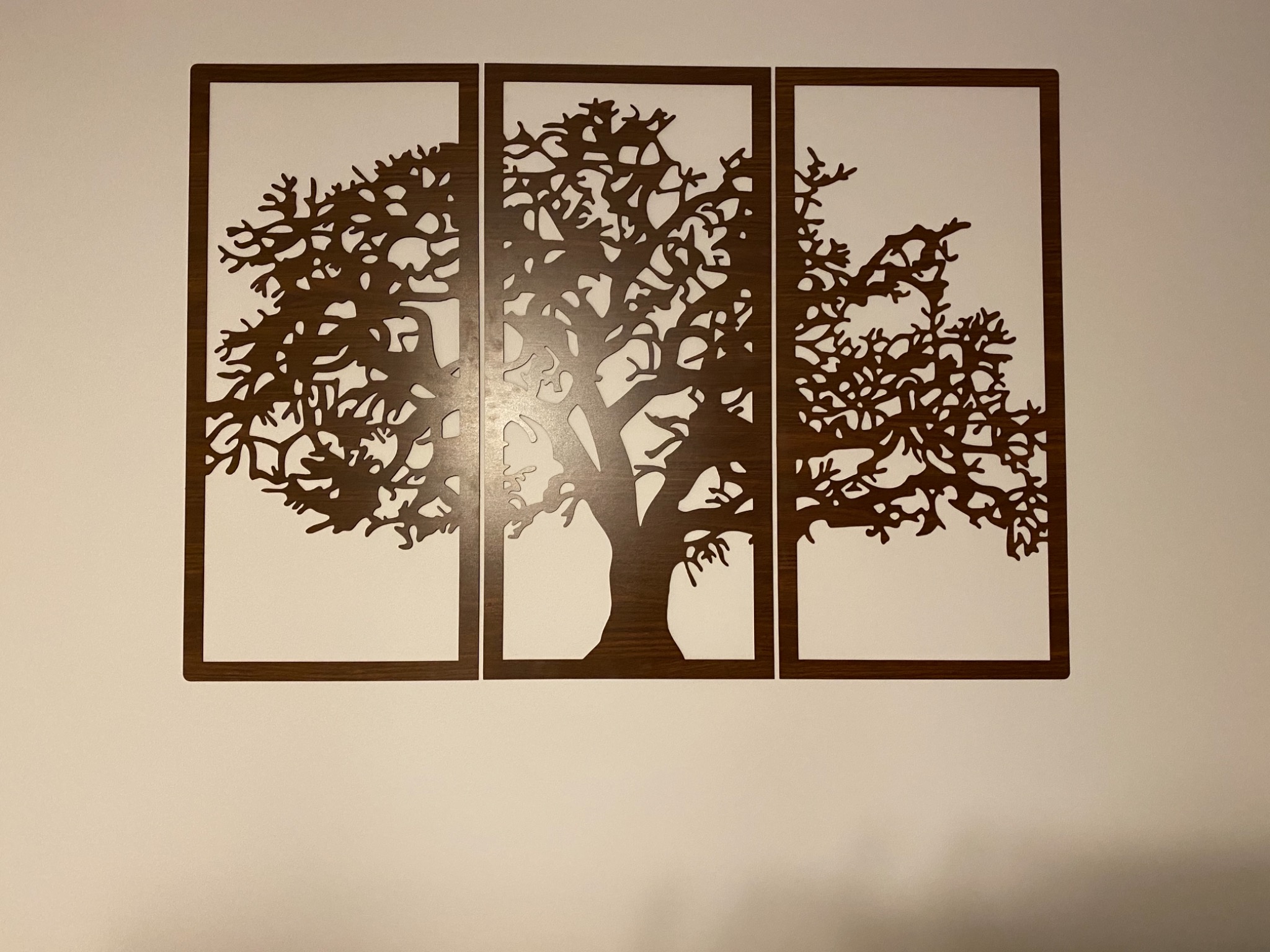 Dekoracja ścienna: trzy drewniane panele przedstawiające stylizowany, wycięty laserowo motyw drzewa na białym tle ściany.