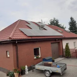 Czerwony dach z panelami słonecznymi na dwuspadowym dachu domu z cegły i garażem, widok z poziomu gruntu w pochmurny dzień.