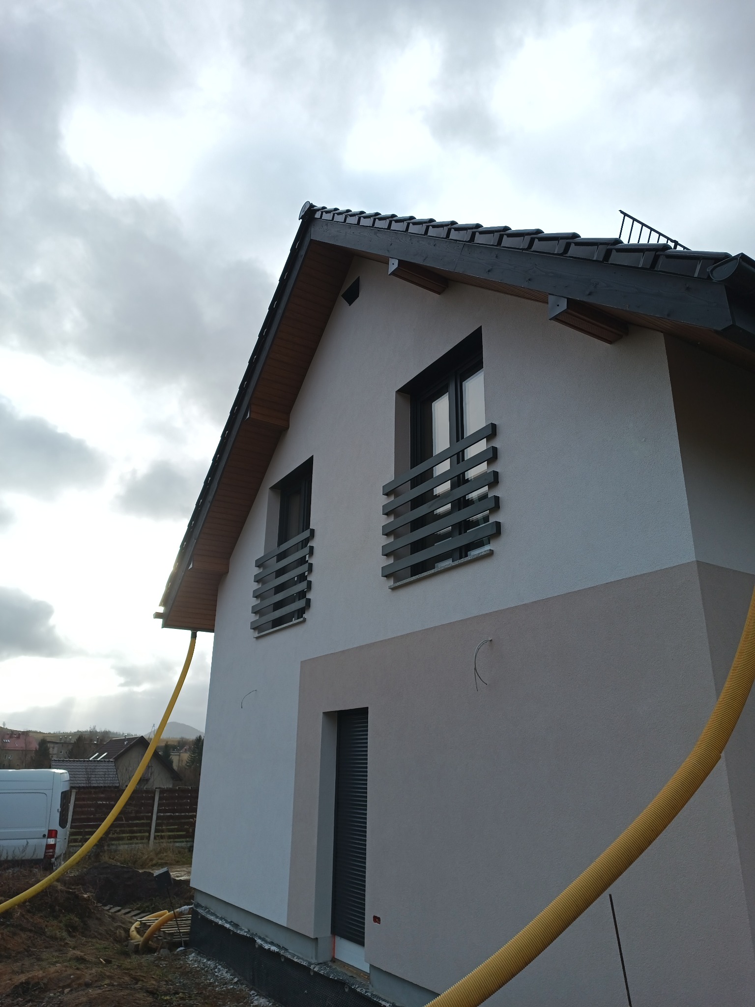 Dwukolorowa elewacja domu jednorodzinnego z czarnymi oknami i żółtym wężem wentylacyjnym w trakcie prac wykończeniowych.