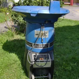 Niebieski rozdrabniacz do wełny mineralnej Isofaccer na trawniku przed budynkiem.