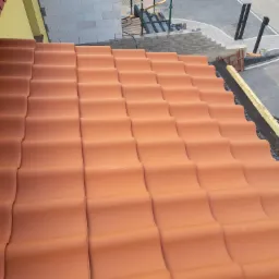 Ułożona dachówka ceramiczna w odcieniach terakoty, widok z góry na fragment dachu w trakcie budowy, z detalami konstrukcyjnymi i elementami otoczenia.