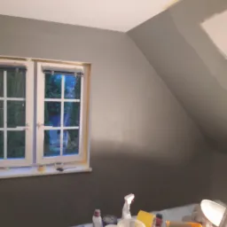 Świeżo pomalowane szare poddasze w Lidzbarku Warmińskim z oknem i narzędziami malarskimi na pierwszym planie.