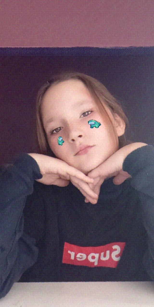 Młoda osoba z filtrami graficznymi na twarzy, opierająca brodę na dłoniach, ubrana w ciemną bluzę z czerwonym napisem.