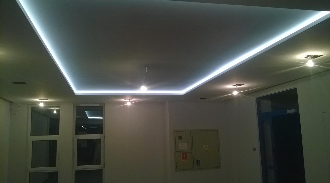 Nowoczesny sufit podwieszany z oświetleniem LED w kształcie prostokąta, uzupełniony punktowymi lampami halogenowymi w nowym, jasnym pomieszczeniu.