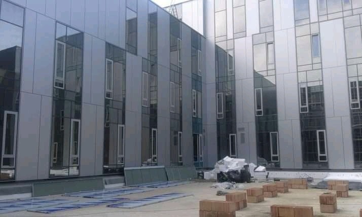 Montaż elewacji z paneli aluminiowych i szklanych okien w nowoczesnym budynku, widoczne materiały budowlane i cegły na placu budowy.