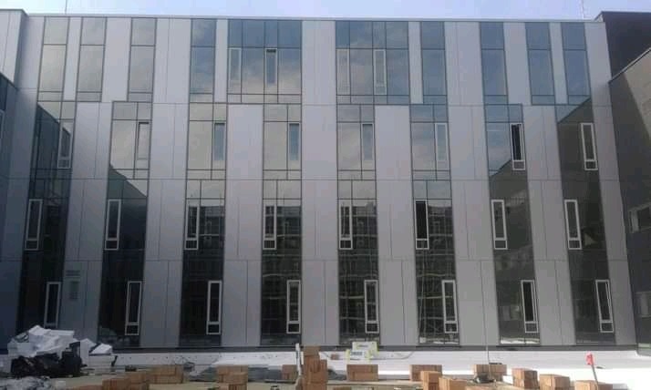 Elewacja budynku biurowego z panelami w odcieniach szarości i licznymi oknami, widoczne materiały budowlane na pierwszym planie.