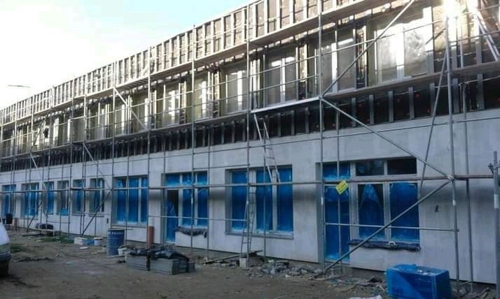 Budynek wielorodzinny w trakcie prac elewacyjnych, widoczne rusztowania, zabezpieczone okna folią, świeżo położony tynk strukturalny.